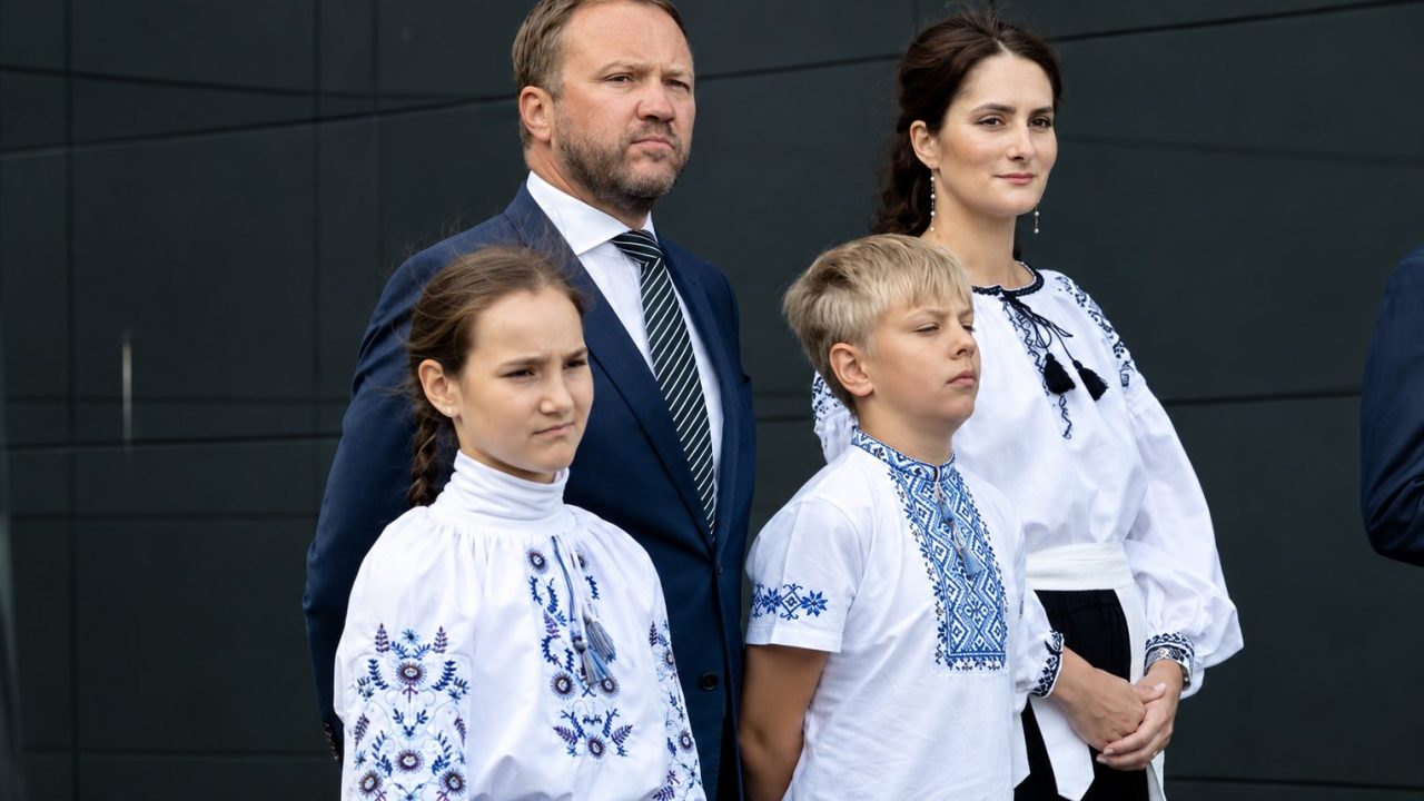 Participants of the flag-raising ceremony in Tallinn: a man in a dark suit, two children and a woman in embroidered shirts