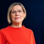 Portrait of a woman with glasses in a red top against a dark blue background