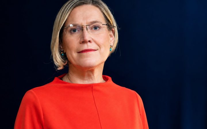 Portrait of a woman with glasses in a red top against a dark blue background